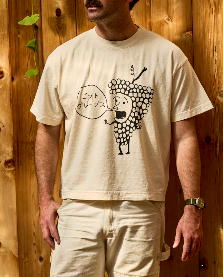 An off-white, unisex oversized Got Grapes T-Shirt featuring a graphic of a cartoon grape character with a speech bubble containing Japanese text.