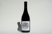 A dark glass wine bottle with a white label featuring a circular black dot pattern, set against a plain white background with a left shadow, showcases Broc Cellars 2022 Trousseau Zin.