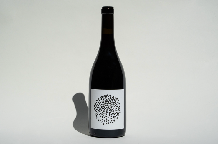 A dark glass wine bottle with a white label featuring a circular black dot pattern, set against a plain white background with a left shadow, showcases Broc Cellars 2022 Trousseau Zin.