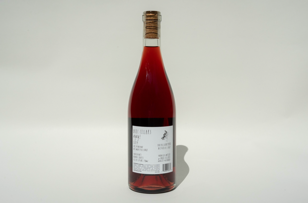 A clear glass bottle of 2024 Ayay! red wine from Broc Cellars, sealed with a cork and featuring a white label with black text, stands upright against a plain white background.