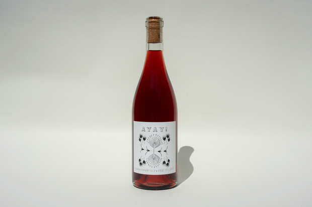 A clear glass bottle of red wine with a cork, labeled 2024 Ayay! by Broc Cellars. The white label shows AVAY! above a black and white artichoke illustration, set against a plain light background.