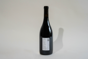 A dark glass bottle of Broc Cellars 2024 Lagrein Red stands upright on a light surface. Its label, showing text, a barcode, and “tech sheet coming soon,” faces the camera as a clear shadow falls to the right.