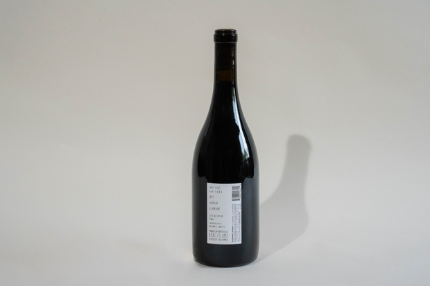 A dark glass bottle of Broc Cellars 2024 Lagrein Red stands upright on a light surface. Its label, showing text, a barcode, and “tech sheet coming soon,” faces the camera as a clear shadow falls to the right.