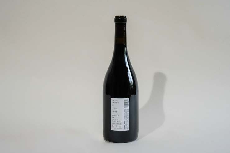 A dark glass bottle of Broc Cellars 2024 Lagrein Red stands upright on a light surface. Its label, showing text, a barcode, and “tech sheet coming soon,” faces the camera as a clear shadow falls to the right.