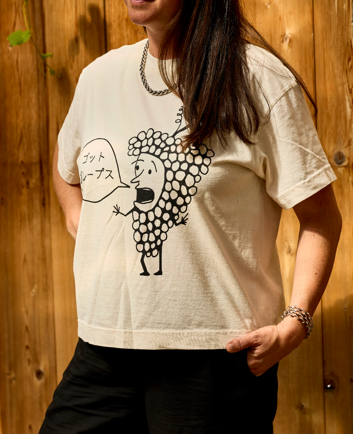 A person wearing an off-white, unisex oversized Got Grapes T-Shirt featuring a line-art graphic of a cartoon grape character speaking Japanese text in a speech bubble.