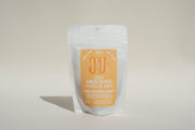 A white stand-up pouch with an orange label reading "Amore Bianco + Yami Yami Pâte de Vin" by Broc Cellars stands upright on a neutral background, suggesting a skin-contact white wine, with extra information beneath.