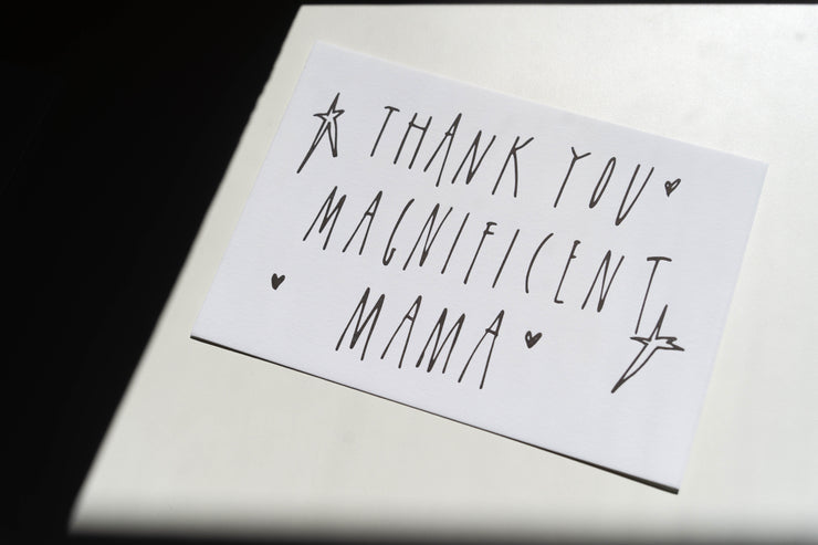 A Broc Cellars Mothers Day Packs card features handwritten THANK YOU MAGNIFICENT MAMA in uppercase letters, decorated with small hearts and stars, and placed on a light-colored surface.