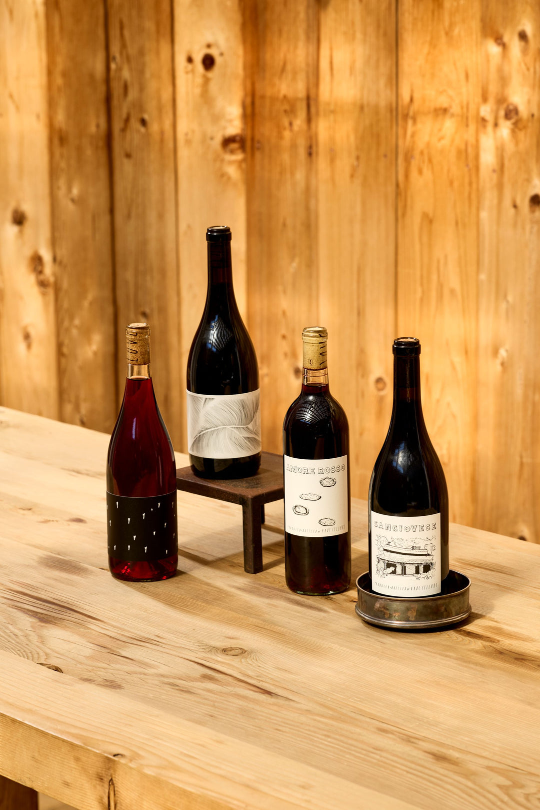 Four bottles of Broc Cellars Essential Reds Pack red wine arranged on a wooden surface, ideal for a dinner party.