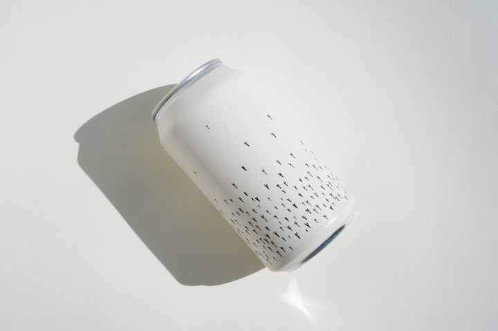 The Broc Cellars Love Sparkling Can Pack features a white aluminum can with minimalist black arrow-like shapes near the bottom, set on a white surface with left-side shadow—ideal for enjoying refreshing everyday sparkling wine.