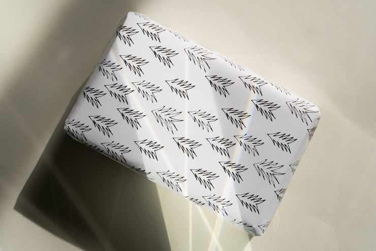 A rectangular gift box from a 10-pack features Broc Cellars Conifer wrapping paper, showcasing a white base with a striking black zigzag. Placed on a light surface in sunlight, it casts enchanting shadows and reflections that add to its allure.